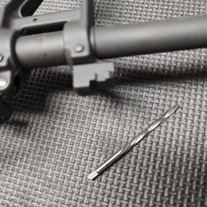A close-up of an AR15 Front Sight Base with a Taper Pin Reamer on a textured surface.