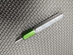 A SOTAR Enhanced AR15 Extractor with a green handle rests on a textured gray surface.