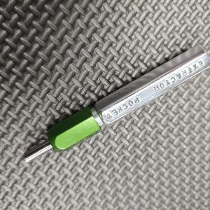 A SOTAR Enhanced AR15 Extractor with a green handle rests on a textured gray surface.