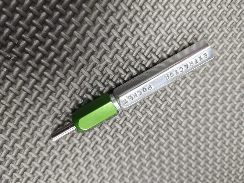A SOTAR Enhanced AR15 Extractor with a green handle rests on a textured gray surface.