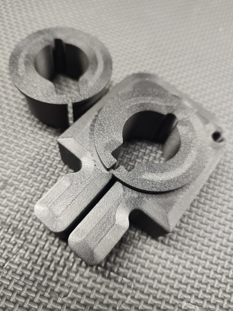 Two black Magazine Button Install Tools, 3D-printed with circular cutouts and slots, rest on a textured dark surface.
