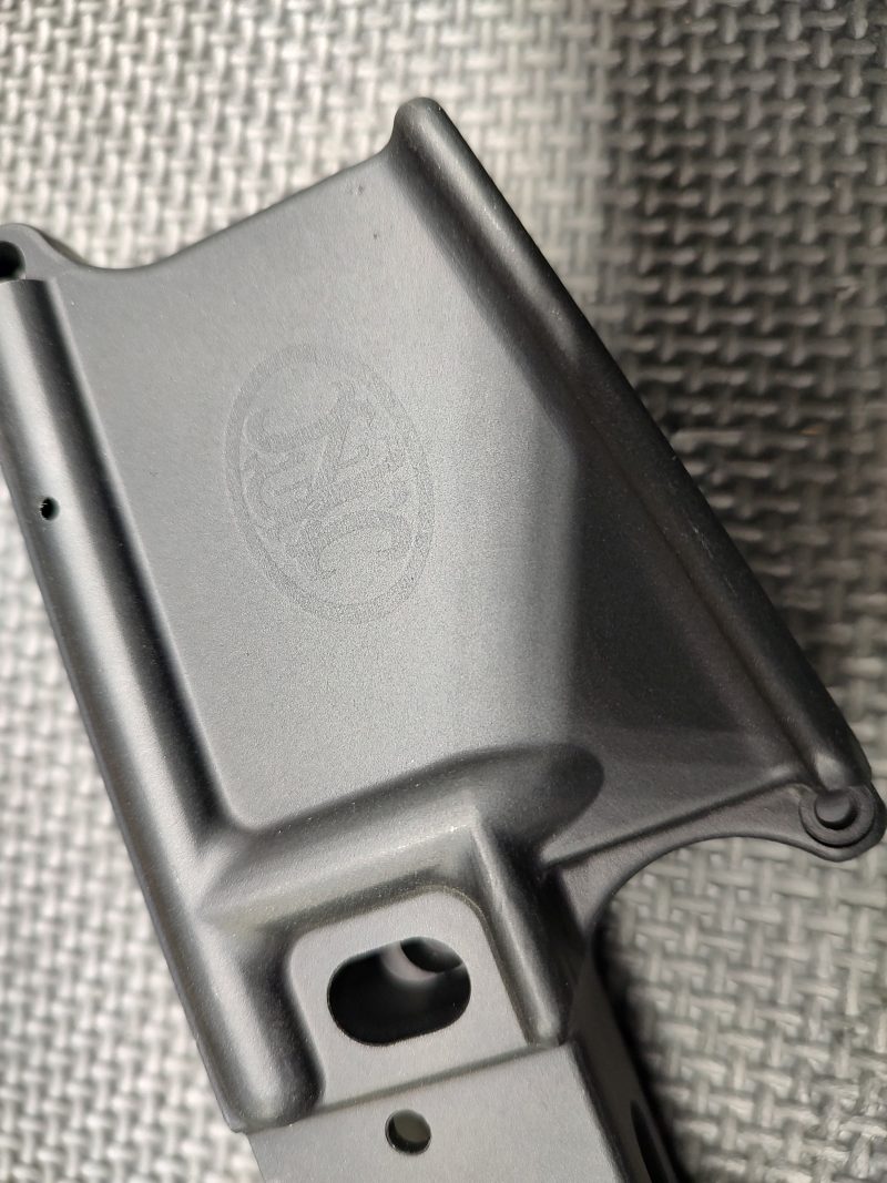 Close-up of a Stripped FN15 Lower Receiver - Fully Inspected and Gauged in matte gray, displaying a faint FN logo, set on a textured metal surface.