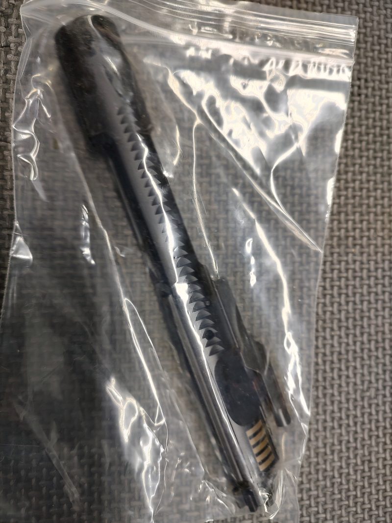 A lightly used AR15/M16 SOLGW BCG is sealed in a clear plastic bag on a textured gray surface.