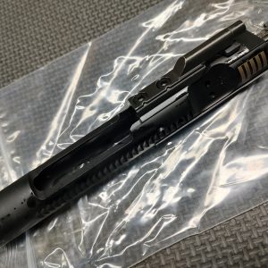 A Lightly Used - AR15/M16 SOLGW BCG rests on a clear plastic zip bag atop a textured gray surface.