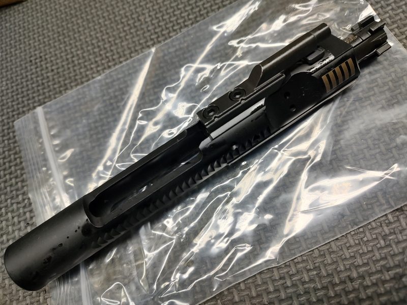 A Lightly Used - AR15/M16 SOLGW BCG rests on a clear plastic zip bag atop a textured gray surface.