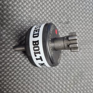 A SOTAR AR15 NEW Bolt Support Ring NOGO Gauge with a textured grip and multi-toothed metal head is shown on a black textured surface.