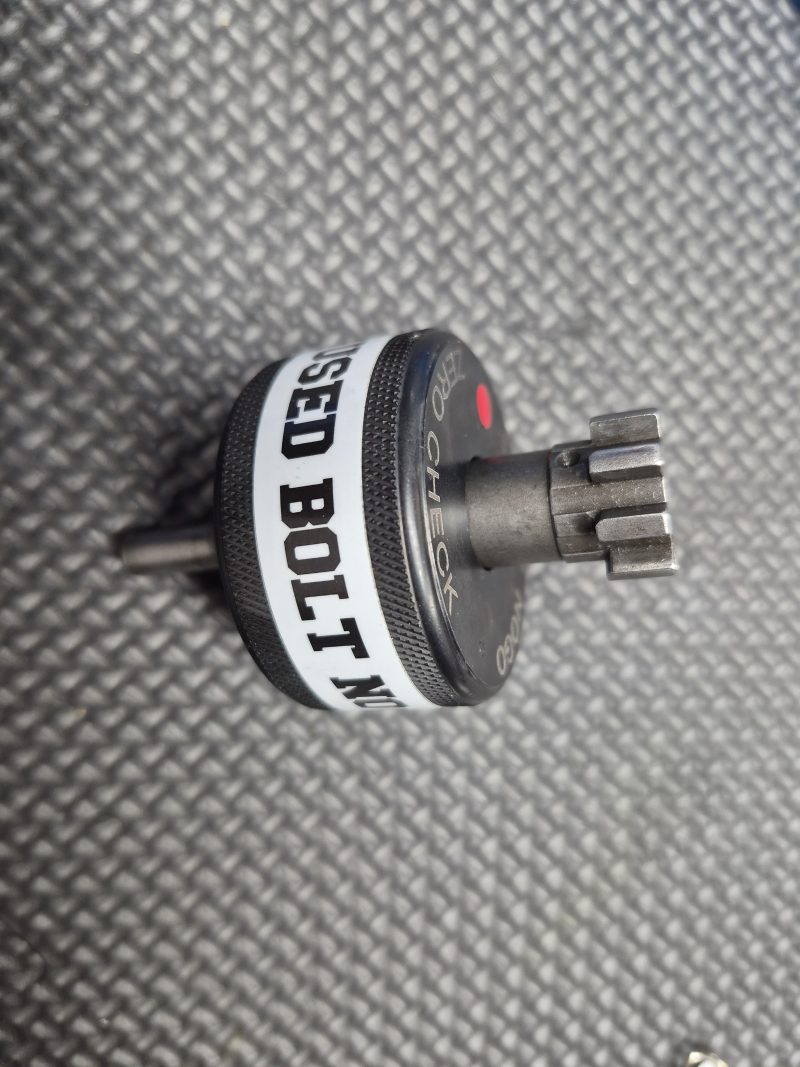 A SOTAR AR15 NEW Bolt Support Ring NOGO Gauge with a textured grip and multi-toothed metal head is shown on a black textured surface.