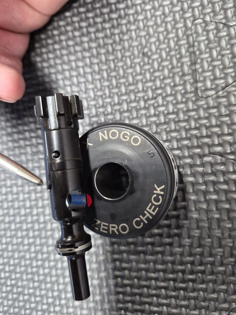 A close-up of the SOTAR AR15 NEW Bolt Support Ring NOGO Gauge, labeled "NOGO" and "ZERO CHECK," sits on a textured black surface with a hand and pen in the background.