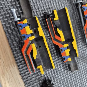 Two EDM CUT - CUTAWAY M16 Bolt Carrier Groups with colored cross-sections highlighting their internal pathways and chambers are placed on a textured black mat.