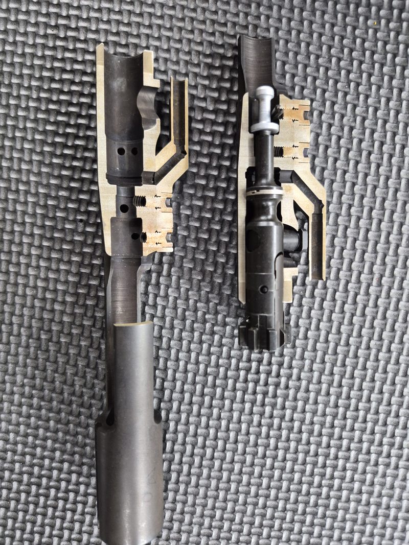 Cross-section view of two EDM CUT - CUTAWAY M16 Bolt Carrier Groups displayed on a textured gray mat, showcasing internal mechanisms and components.