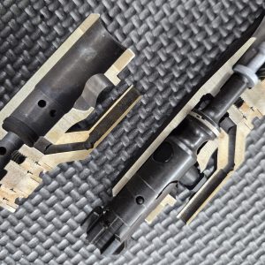 Two EDM CUT - CUTAWAY M16 Bolt Carrier Groups are displayed on a textured black surface, revealing their internal components and mechanisms.