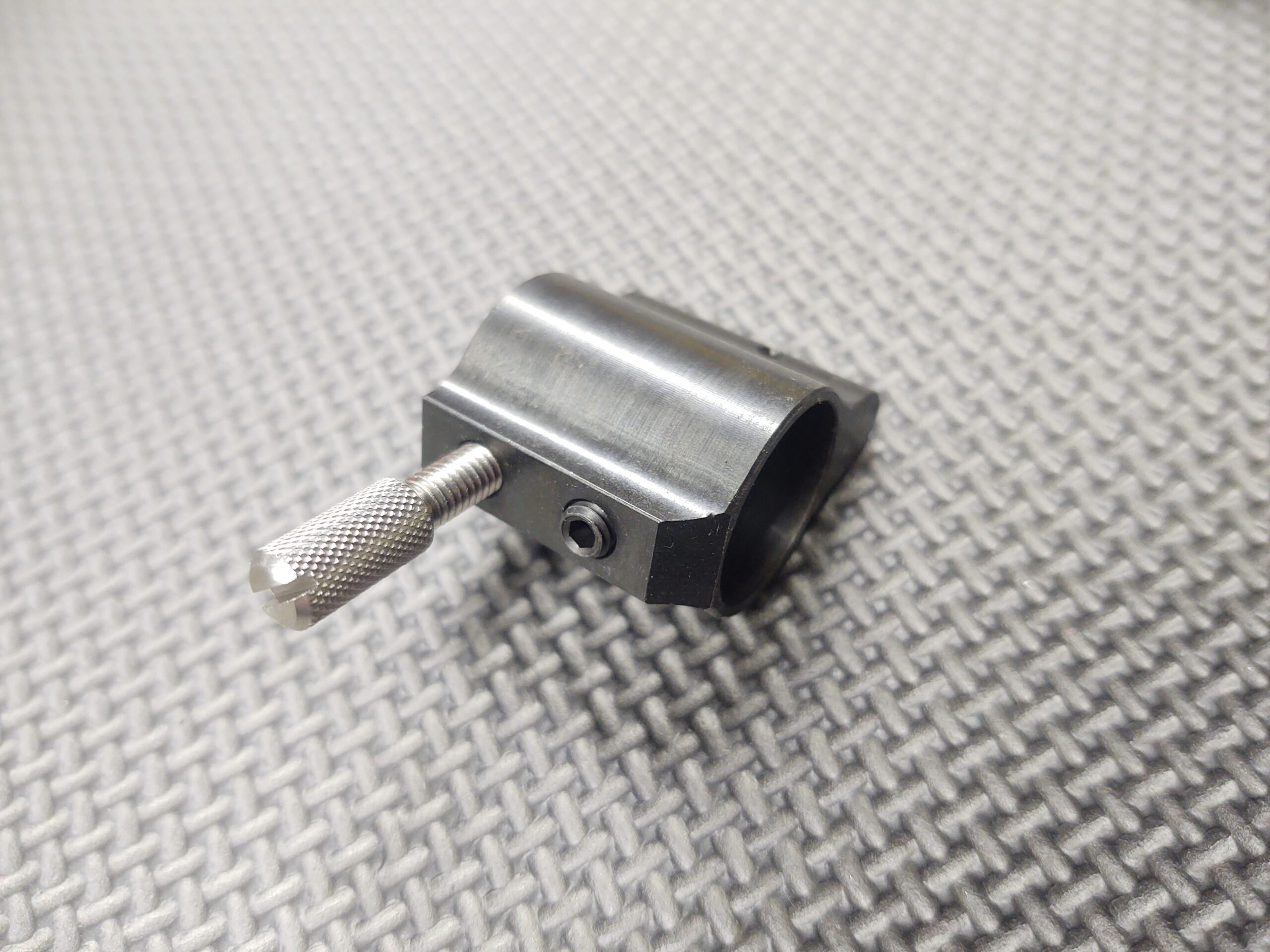 A small piece of metal with a 10-32 Gas Block/Gas Port Installation Thumb Screw on it.