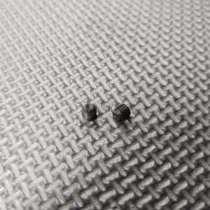 A pair of 10-32 Knurled Tip Gas Block Set Screws on a metal surface.