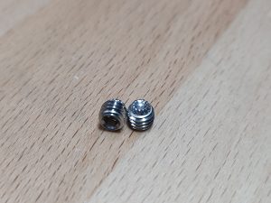Two 10-32 "18-8 Stainless Steel" Knurled Tip Gas Block set screws on a wooden surface, one larger with ridges and the other smaller with a rounded top.