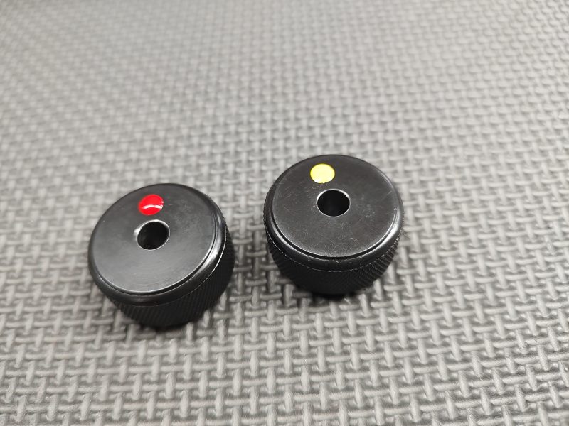 Two small black knobs with colored indicators (red and yellow) on a textured grey surface. SOTAR AR15 Bolt Tail Gauge Set - BACKORDER
