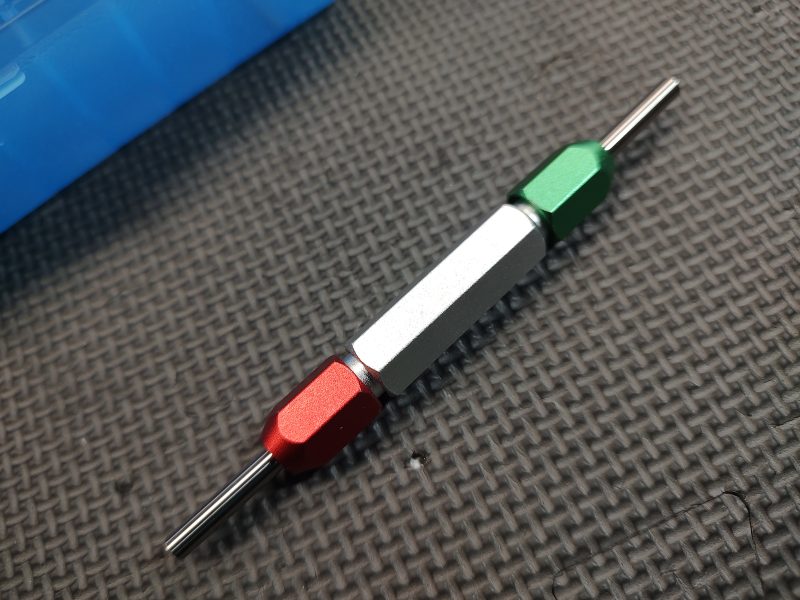 A SOTAR AR15 BCG 3 Bore & Gas System Gauge Set with Imported Handle - BACKORDER, with a red, white, and green segmented handle, lying on a textured black surface.