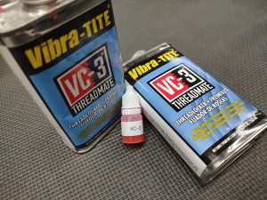 Two containers of the AR Barrel Bedding Shim Kit - No Loctite 620 and a small bottle of VC-3 are placed on a textured surface. The containers feature a black and blue label with yellow and white text.