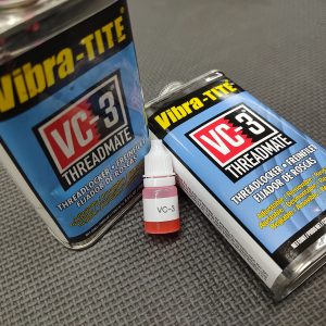 Two containers of the AR Barrel Bedding Shim Kit - No Loctite 620 and a small bottle of VC-3 are placed on a textured surface. The containers feature a black and blue label with yellow and white text.