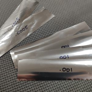 AR Barrel Bedding Shim Kit - No Loctite 620 metallic foil strips, each labeled with varying thickness measurements, lay on a textured gray surface.
