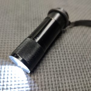 A green AR Upper Receiver Illumination Tool - Green (Copy) emitting a bright beam of light sits on a textured grey surface.