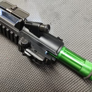 Close-up view of the AR Upper Receiver Illumination Tool - Green (Copy) with an anodized handguard, placed on a textured surface.