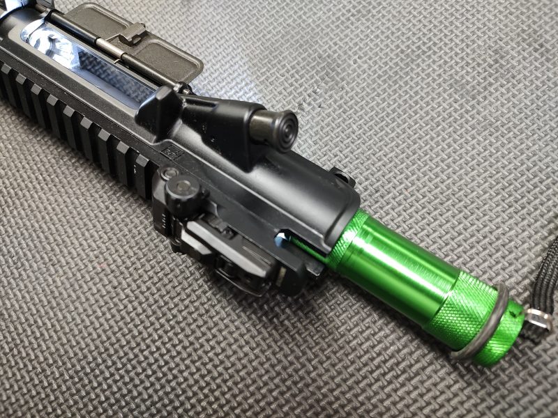 Close-up view of the AR Upper Receiver Illumination Tool - Green (Copy) with an anodized handguard, placed on a textured surface.