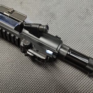 Close-up of a black AR Upper Receiver Illumination Tool - Green, featuring an attached flashlight, resting on a textured surface.