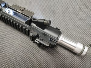 Close-up of an AR Upper Receiver Illumination Tool - Green. The image highlights the ejection port, charging handle, and forward assist on a firearm placed on a textured grey surface.