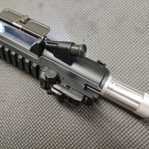 Close-up of an AR Upper Receiver Illumination Tool - Green. The image highlights the ejection port, charging handle, and forward assist on a firearm placed on a textured grey surface.