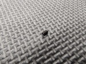 A 4-40 Set Screw lies on a grey textured surface with a grid-like pattern.