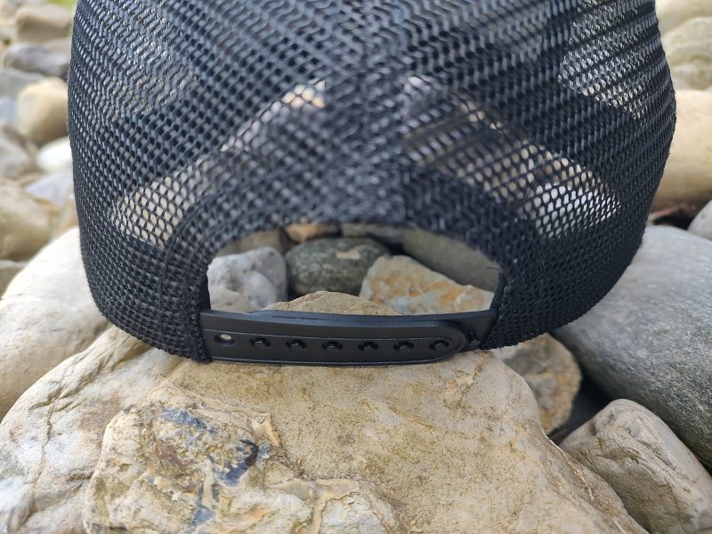 A close-up view of the backside of a black mesh cap with an adjustable strap, placed on a collection of gray stones.