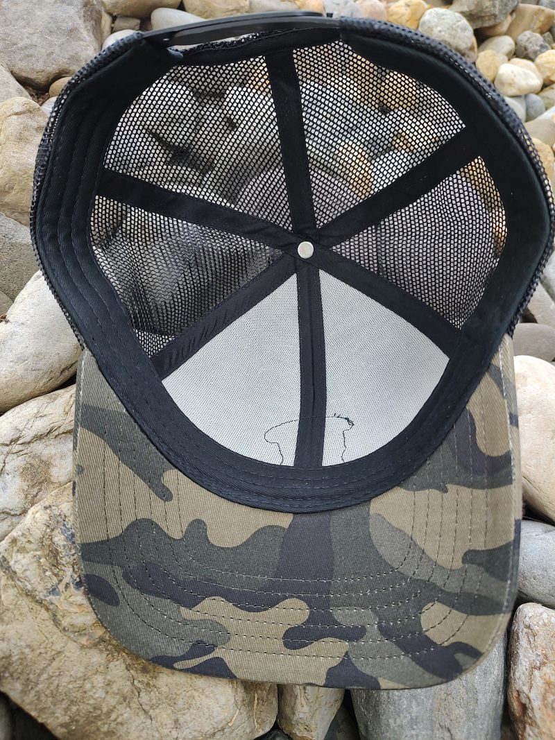 An upside-down camouflage baseball cap with a mesh back rests on a pile of rocks.