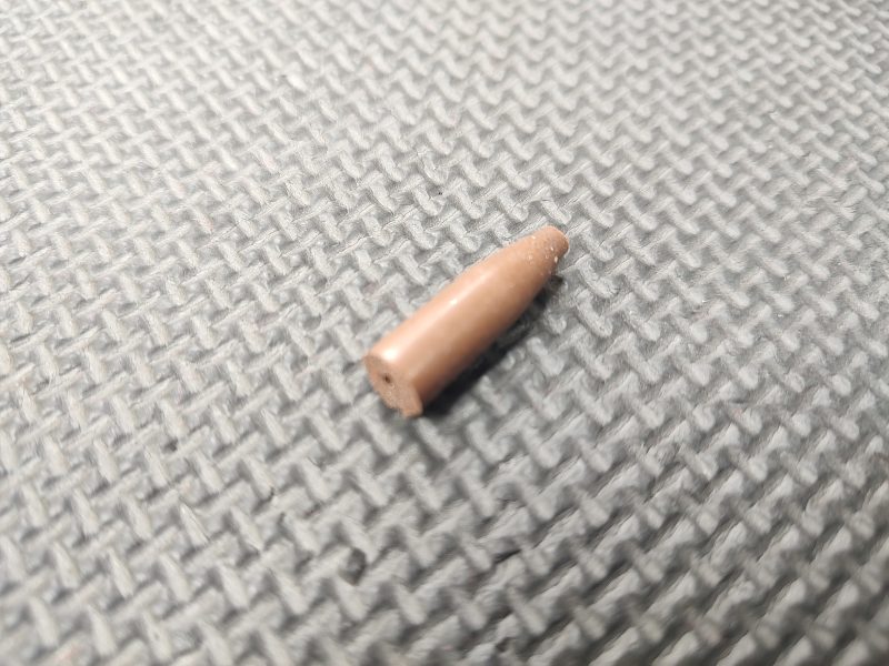 An item from the AR15 Feed Ramp Cut & Polish Kit, a small brown cylindrical object with a pointed tip, lies on a textured gray surface.