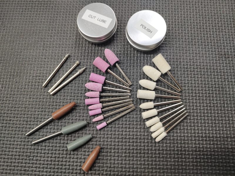 Various dental grinding and polishing tools are neatly arranged on a textured surface, alongside two containers labeled "CUT LUBE" and "POLISH" from the AR15 Feed Ramp Cut & Polish Kit.