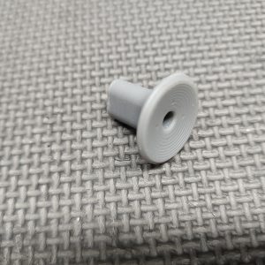 A compact light gray plastic Magazine Button Install Tool with a central hole rests on a textured gray surface.