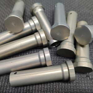 A pile of cylindrical metal rods with flat ends and circular grooves, lying on a textured dark surface.