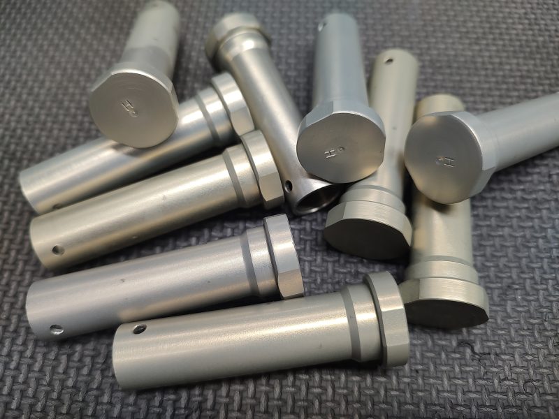 A pile of cylindrical metal rods with flat ends and circular grooves, lying on a textured dark surface.